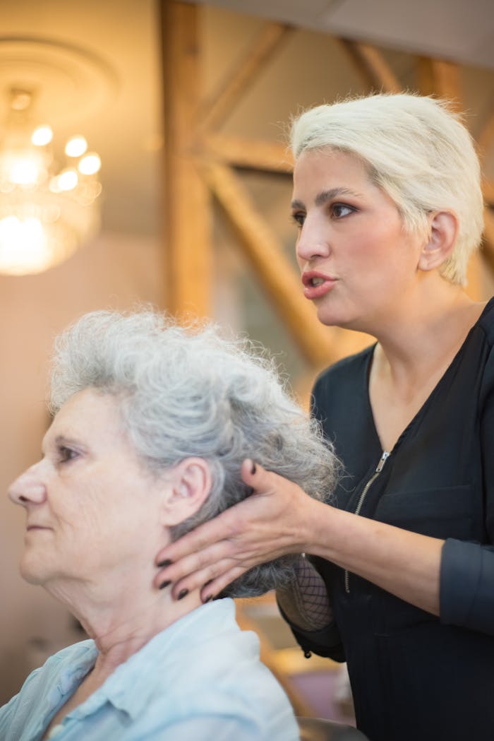 Hairdresser providing a haircut to an elderly woman in a salon setting.
