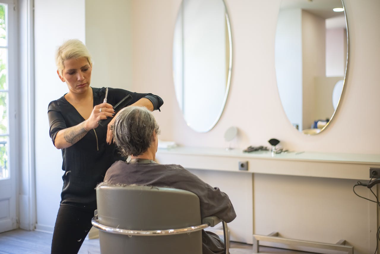 A hairdresser skillfully cuts an elderly woman's hair in a modern salon with mirrors and a comfortable barber chair.